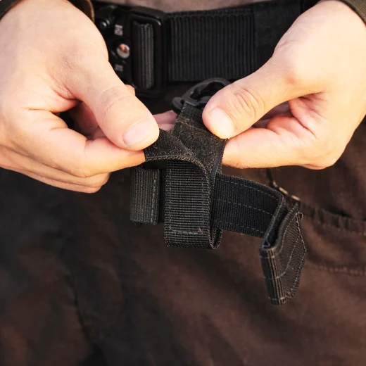 Hands attaching a black glove holder strap to a belt loop for carrying work or winter gloves