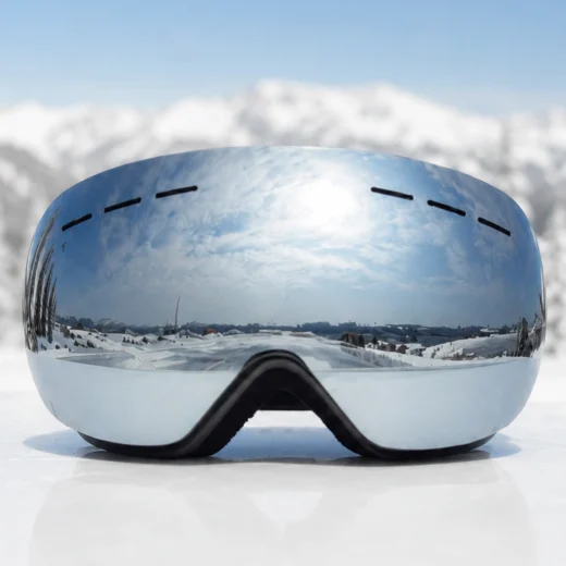 front view of silver mirror snow goggles against a snowy mountain background