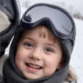 Child wearing black childrens ski goggles with a grey lens during a snowy outdoor trip